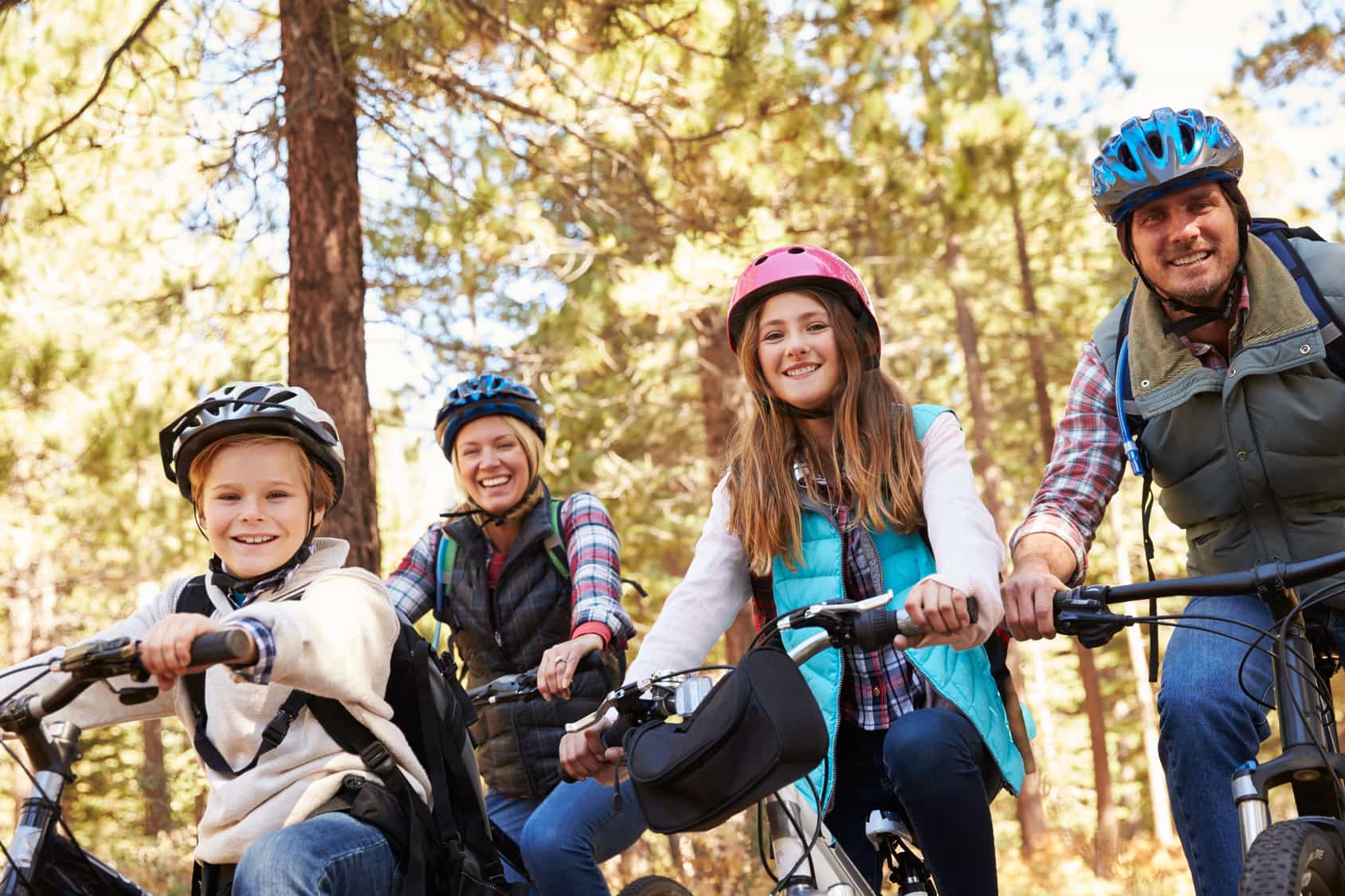 Familienurlaub mit dem Rad: Vater, Mutter, Tochter, Sohn auf Mountain-Bikes lächeln in die Kamera.