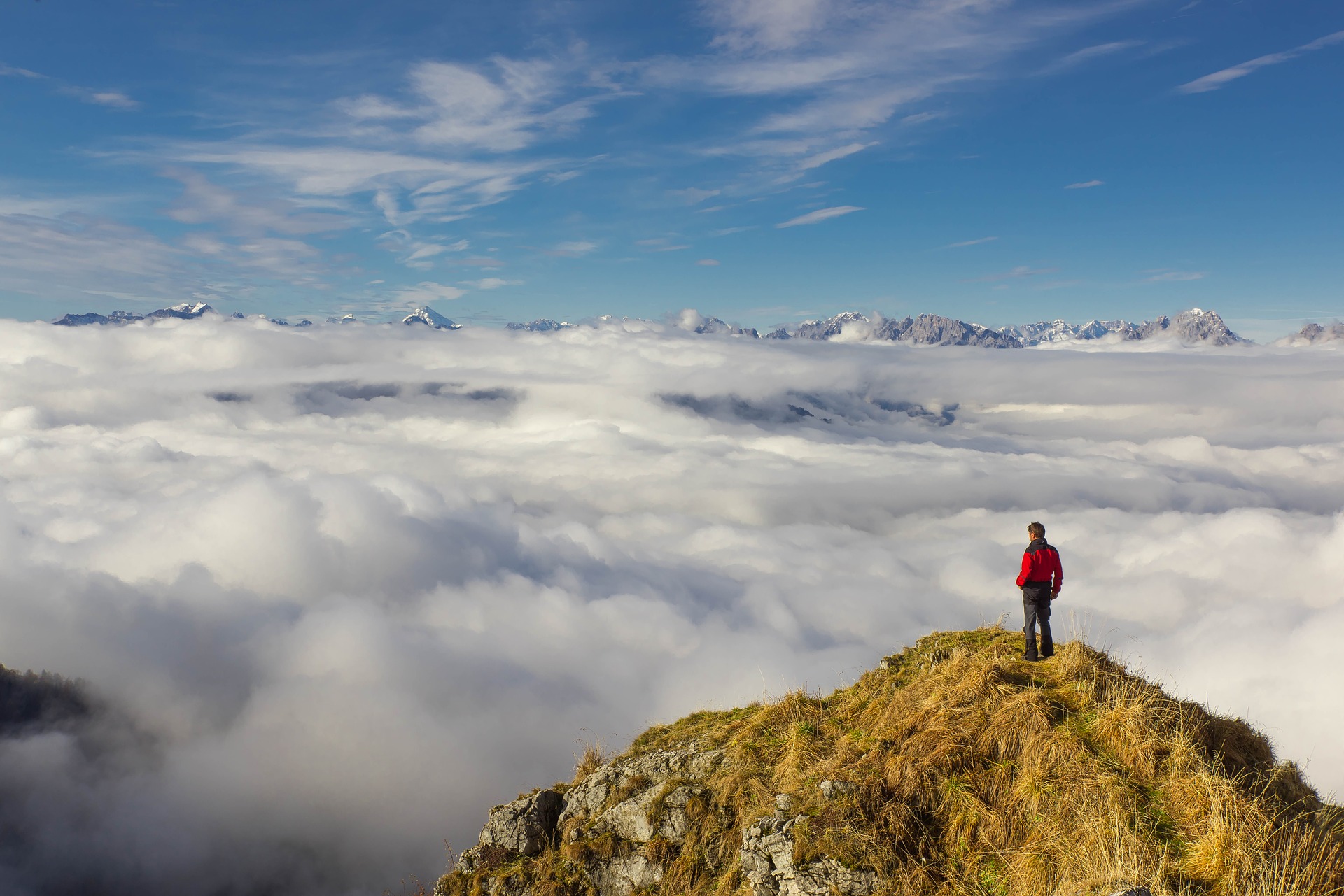 Ein Mann steht über den Wolken auf einem Berggipfel.