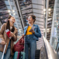 Zwei Frauen am Flughafen halten ihre Flugtickets bereit.