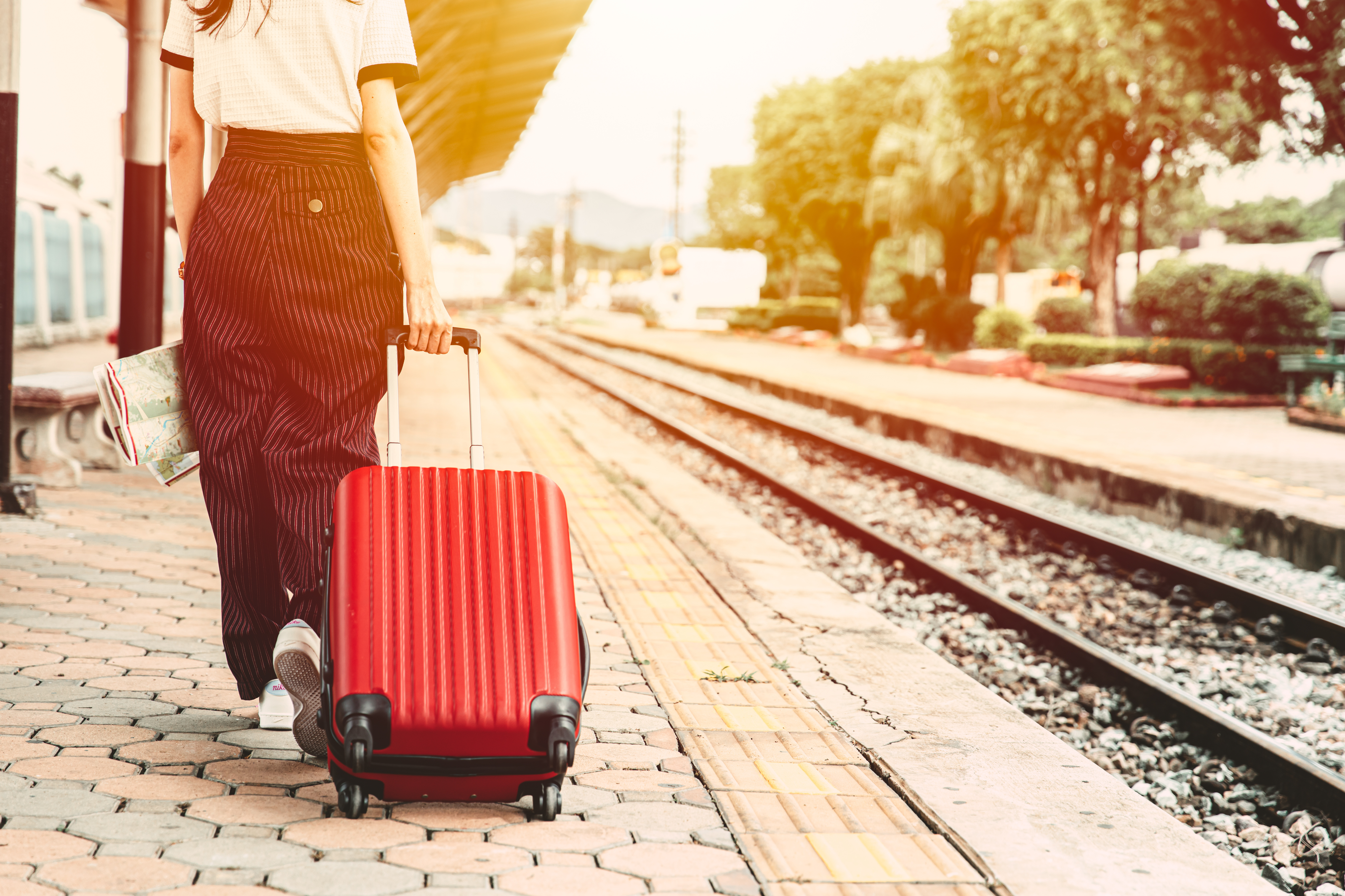 Frau mit rotem Rollkoffer und Stadtplan geht auf einem Bahnsteig entlang in Richtung Gleis.